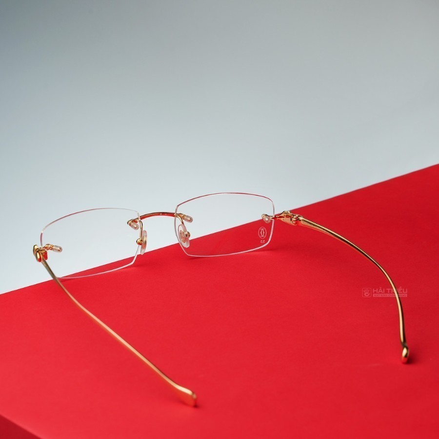 Chiếc kính gọng vàng không viền của Cartier đang được bày trí trên chiếc bàn đỏ